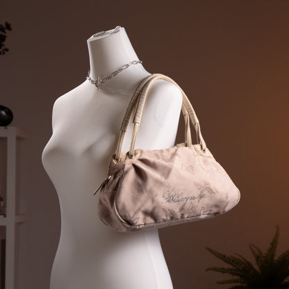 Blumarine Y2K Baguette Bag by Anna Molinari – blush beige nylon with tone-on-tone butterfly jacquard print, rhinestone crystal "Blumarine" script logo, dual rolled leather top handles with gold ring hardware, zip closure, Made in Italy, shown on dress form