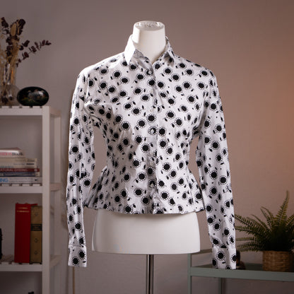 Front view of the flawless archival Azzedine Alaïa black and white daisy print cotton poplin peplum blouse highlighting the structured waist on a museum mannequin.
