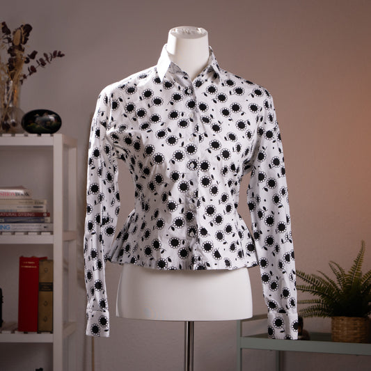 Front view of the flawless archival Azzedine Alaïa black and white daisy print cotton poplin peplum blouse highlighting the structured waist on a museum mannequin.

