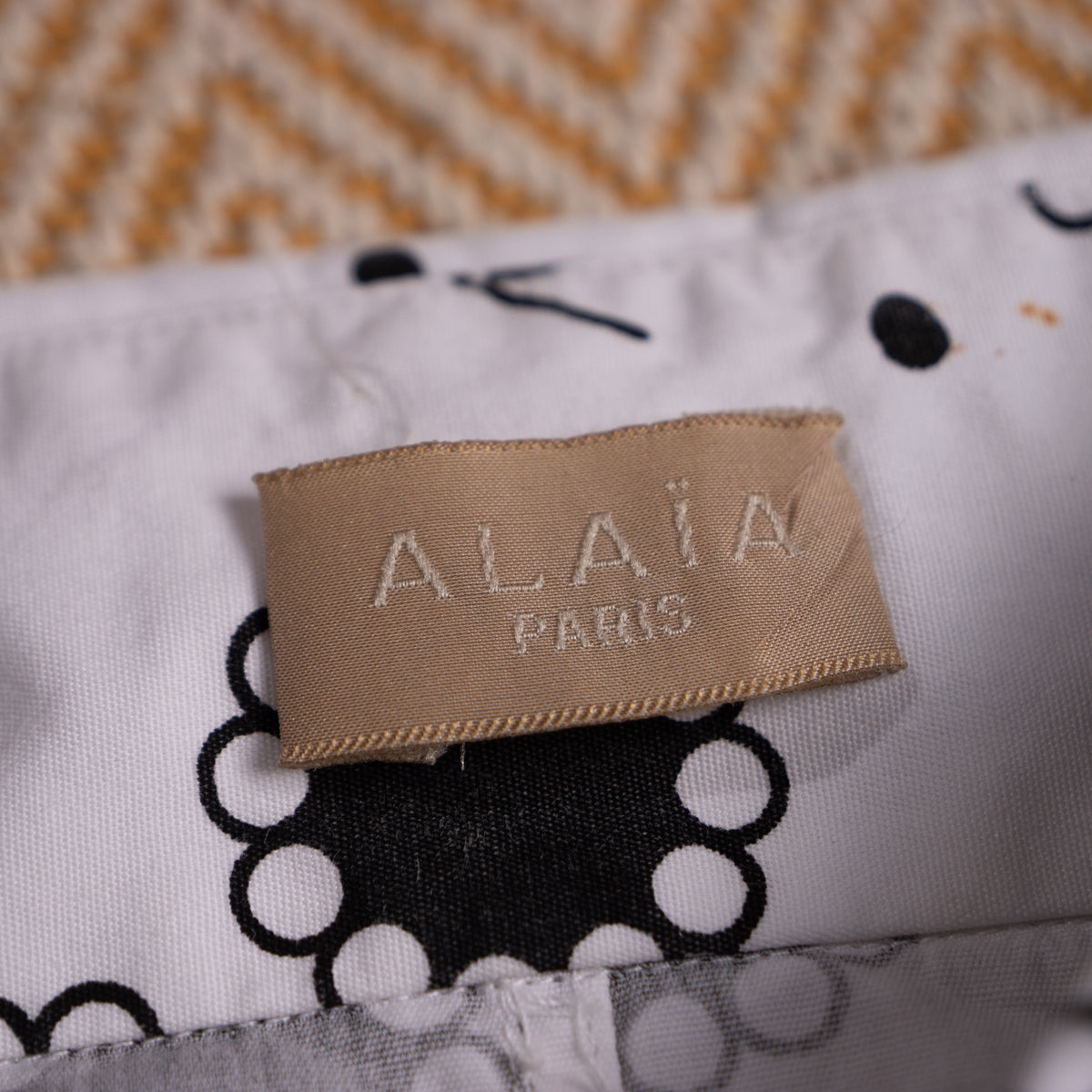Close-up view of the light-beige silk-woven Alaïa Paris neck label attached to the optic white printed cotton fabric grain.