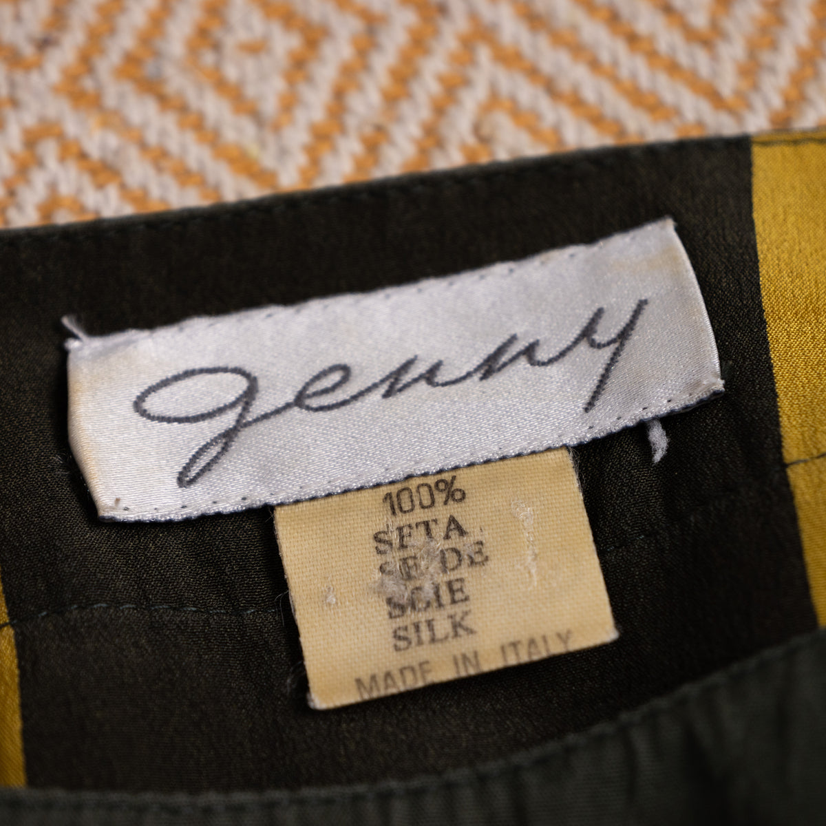 Close-up of the vintage archival Genny woven script neck label representing the early 1970s Gianni Versace design era with 100 percent silk tag.
