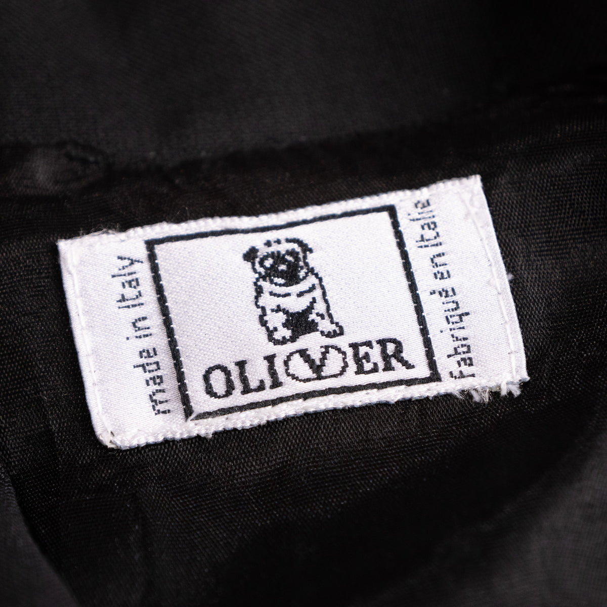Close-up interior view of the woven white Oliver by Valentino label featuring the signature pug logo and Made in Italy stamp.