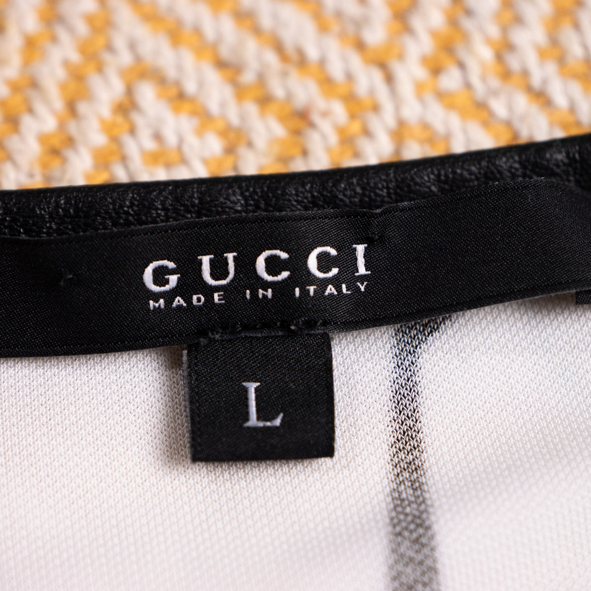 Close-up interior view of the woven black satin Gucci Made in Italy main label with the attached size L drop tag on the leather piping seam.
