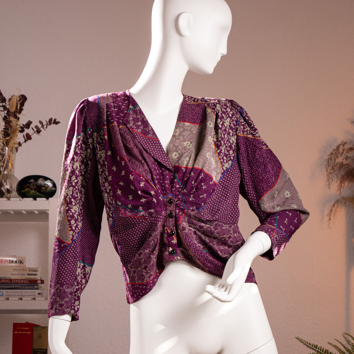 Front view of the flawless archival Emanuel Ungaro Parallèle patchwork print silk jacquard blouse highlighting the draped V-neckline and faceted black buttons on a museum mannequin.
