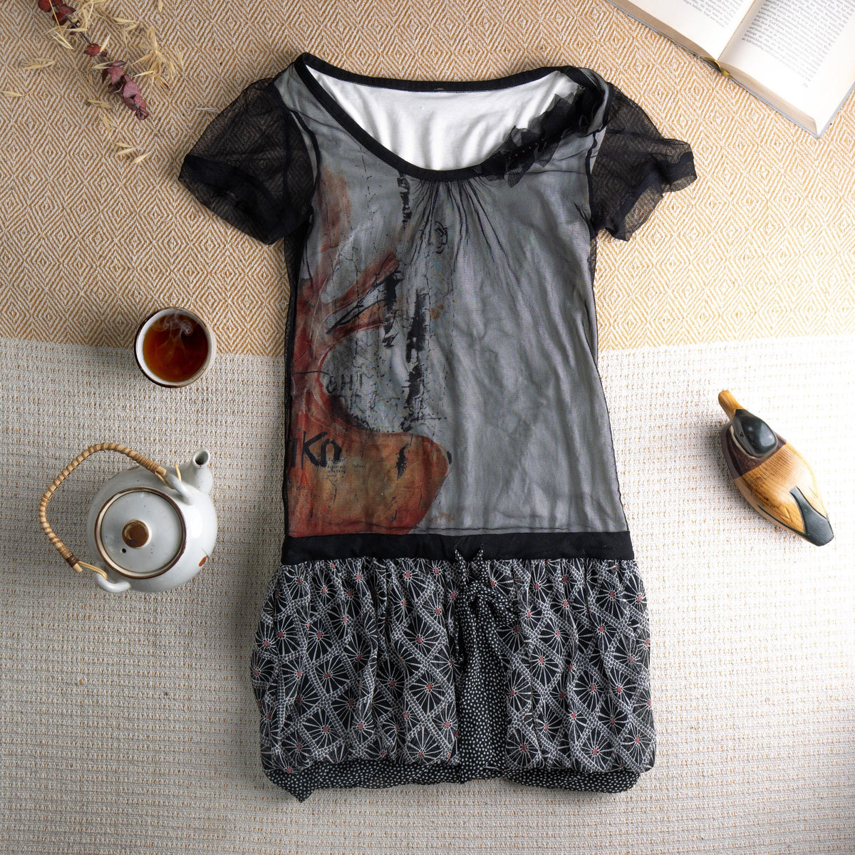 Rare Cop Copine "Geiko" Y2K Archival Mesh Mini Dress – sheer black tulle overlay bodice with large-scale abstract geisha face graphic print in grey, rust and terracotta, black lace short sleeves with floral appliqué at neckline, white jersey underlayer, black waistband, gathered bubble hem skirt in black and white geometric star pattern, avant-garde French designer, flat lay editorial shot