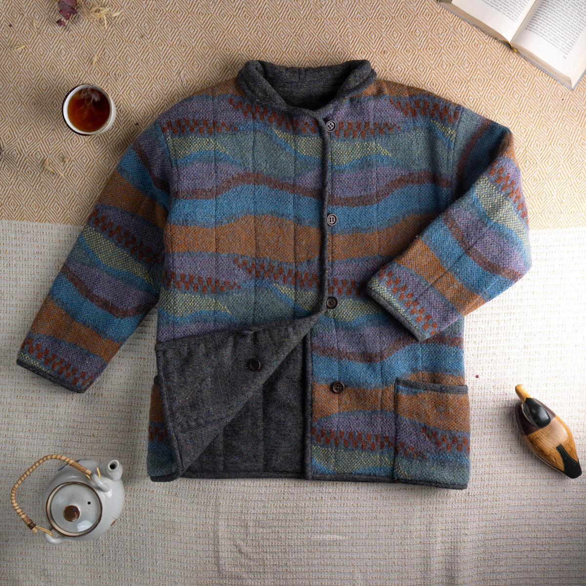 Archival Missoni Early 1990s Orange Label Reversible Fiammato Wave Quilted Jacket – multicolour mohair blend fiammato knit with undulating wave stripe pattern in teal blue, burnt amber, mauve and olive, stand collar, four dark horn button front closure, two patch pockets, reverses to solid charcoal grey herringbone tweed, flat lay editorial shot showing both sides