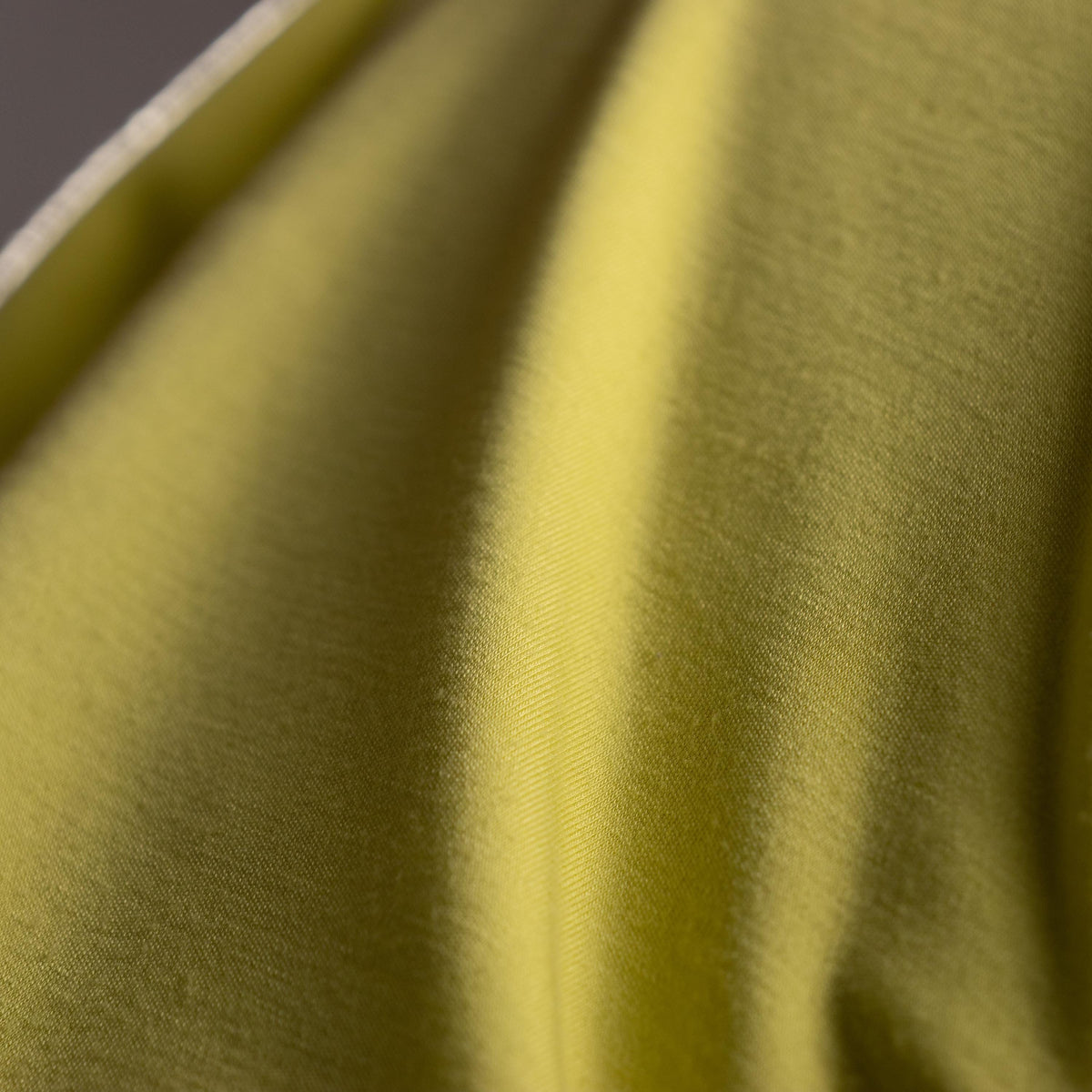 Close-up of green fabric with a subtle pattern. Archival Halston Mainline 2000s Acid Lime Asymmetric Off-Shoulder Mini Dress – saturated acid lime yellow-green stretch satin, single asymmetric diagonal off-shoulder neckline, one long sleeve, body-con mini silhouette, silk lining, Bradley Bayou era, Made in Italy IT 38 XS S, product shot on dress form